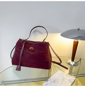Details einer burgunderroten Wildledertasche mit goldener Drehsperre auf Glastisch