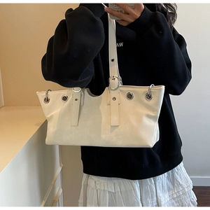 Detail view of white leather tote bag with silver eyelet rivets and adjustable strap