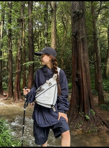 Detail of white waterproof crossbody bag with black straps in outdoor forest setting