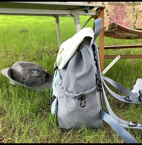 Outdoor camping scene showing a grey sun hat and grey-blue nylon backpack on green grass
