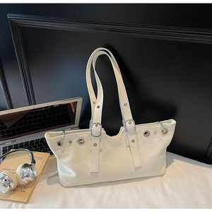 Cream white faux leather tote bag with silver eyelets and adjustable straps on a desk
