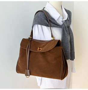 Detailansicht der braunen Wildledertasche mit goldenem Drehverschluss auf Pullover