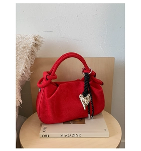 Detail of red suede handbag featuring thick rope knot handle and silver heart charm pendant