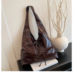 Close-up of glossy wrinkled leather tote bag with a decorative bow and wide shoulder strap