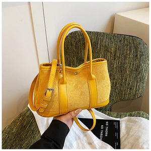 Detail of lemon yellow bucket bag showing suede stitching and adjustable strap in hand
