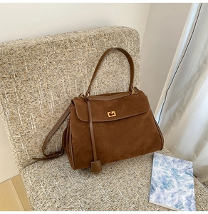 Detail einer braunen matten Ledertasche mit goldenem Drehverschluss auf einem Sessel