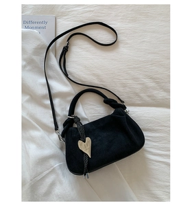 Detail of a black pleated dumpling bag with silver heart pendant and woven top handle