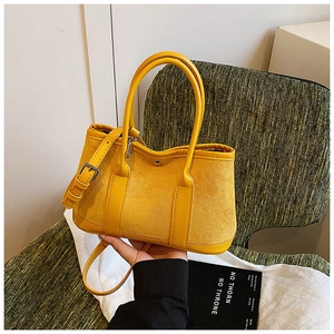 Detail of yellow bucket bag showing suede and smooth leather textures on green chair