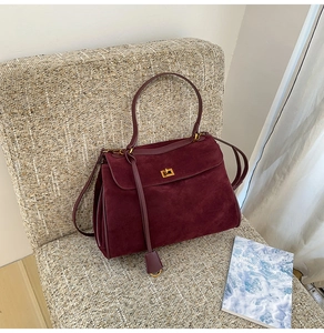 Detail der vintage mattburgunderroten Tragetasche mit goldenem Drehverschluss und Wildleder
