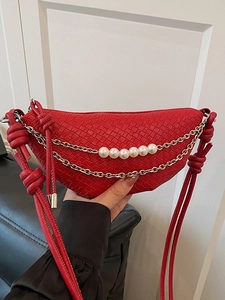 Sac bandoulière demi-lune tressé rouge avec chaîne dorée et perles, porté à la main