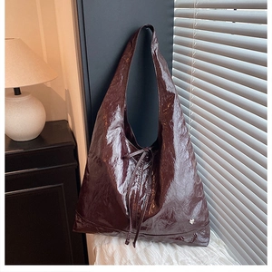 Detail of burgundy glossy tote bag featuring pleated texture and heart-shaped metal charm