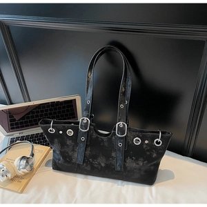 Distressed black tote bag with metallic eyelets and studs in a modern office setup