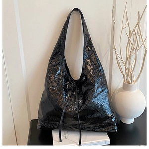 Detail of black glossy patent leather hobo bag with bow decoration and silver heart tag