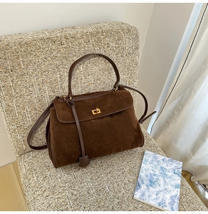 Detailansicht braune Wildledertasche mit goldenem Drehverschluss auf einem Sessel