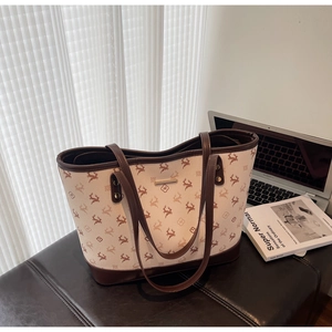Close-up of beige tote bag with deer pattern and brown leather trim on a dark bench