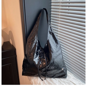 Detail of glossy wrinkled black leather texture and small silver heart metal logo on tote bag