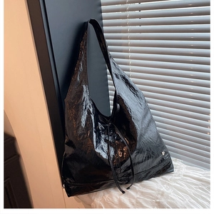 Detail of black glossy crinkled leather tote bag with silver heart logo on white lace