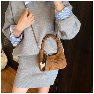 Close-up of brown suede crescent bag with bow detail and heart pendant on model