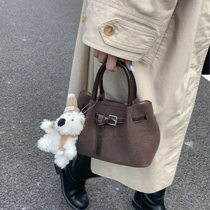 Close-up of textured dark brown bucket bag with a cute white teddy bear charm and strap