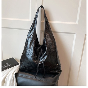 Detail of black glossy hobo bag featuring crinkled texture and silver heart logo