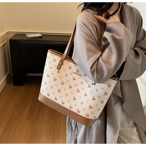 Close-up of beige tote bag with reindeer pattern and brown leather straps in indoor setting