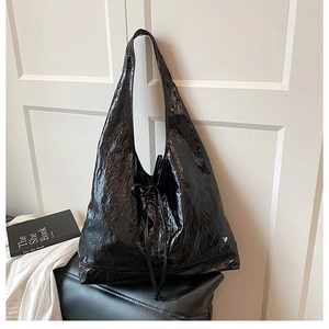 Close-up of black glossy crinkle tote bag with metal heart charm and tie detail