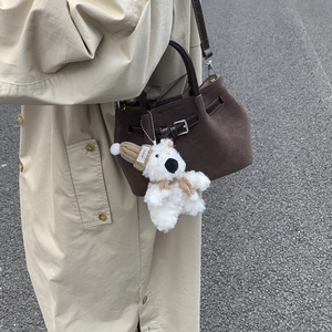Close-up of a plush white teddy bear charm with a knitted hat on a brown leather bag