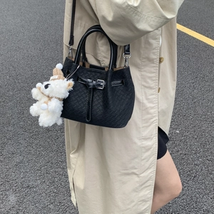 Close-up of black woven bucket bag with silver buckle and polar bear plush charm