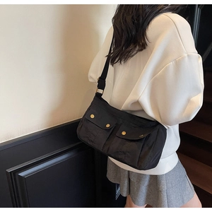 Detail of black nylon shoulder bag featuring twin front pockets and gold snap buttons