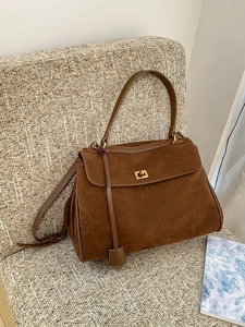 Braune Vintage Wildledertasche mit goldenem Drehverschluss auf grauem Websessel