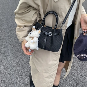 Detail view of black woven texture bag with plush puppy charm and metal buckle