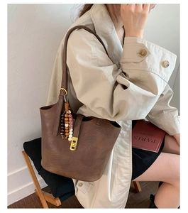 Detail of dark brown retro bucket bag featuring gold buckle and wooden beaded tassel charm