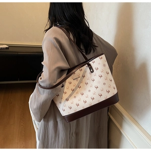 Close-up of large tote bag with deer pattern, contrast leather handles and metal plate