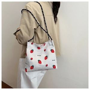 Detail of white strawberry print tote bag with woven shoulder strap and smile lettering
