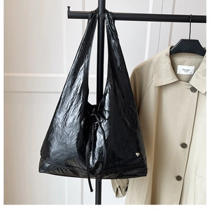 Detail of black patent leather tote bag with drawstring bow and small heart charm