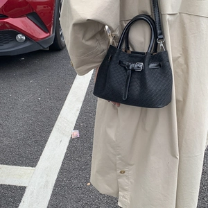Detailed view of a black woven bucket bag styled with a beige trench coat outdoors