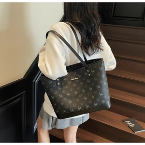 Detail of a large black printed tote bag worn by a model in a modern urban setting