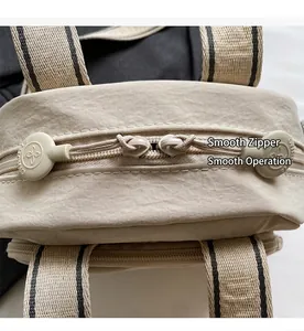 Detail der glatten Doppelreißverschlüsse und gestreiften Riemen dieser beigen Tasche
