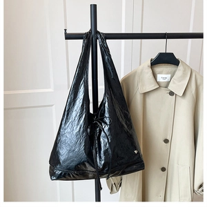 Detail of black glossy tote bag with drawstring design and heart-shaped metal charm