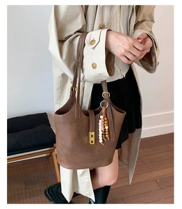 Detail of vintage brown bucket bag featuring gold metal clasp and woven bead charm