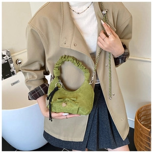 Close-up of green suede crescent bag featuring bow decoration and gold heart charm detail