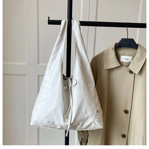 Detail shot of a white pleated tote bag with a bow detail hanging on a metal rack