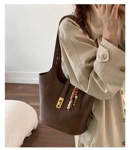 Detail of dark brown leather tote bag with gold metal buckle and beaded charm pendant