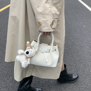 Detail of white woven textured bucket bag featuring a plush charm and metal buckle accent