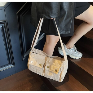Macro detail of beige nylon shoulder bag showing dual front pockets with metal buckles