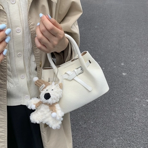 Detail of white woven leather bucket bag with cute plush bear charm on beige coat background