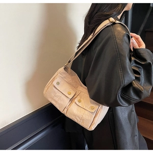 Detail of beige shoulder bag featuring dual cargo pockets and gold metal snap buttons