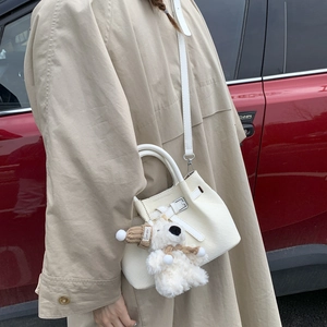 Close-up of white croc-effect bucket bag with cute teddy bear charm and strap