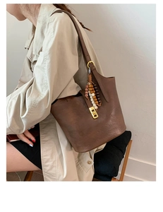 Detailed view of brown leather bucket bag featuring vintage bead tassel and gold lock