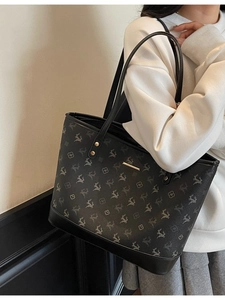 Large black tote bag with gray floral pattern and gold hardware on model shoulder
